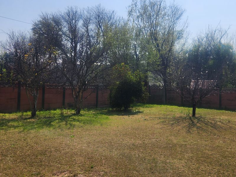 A spacious backyard garden featuring mature trees, a perimeter precast concrete wall, and an elevated water storage tank on a steel stand.