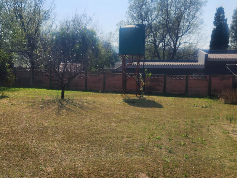 A spacious backyard featuring a lawn, a precast concrete boundary wall, and a water storage tank on a steel stand.
