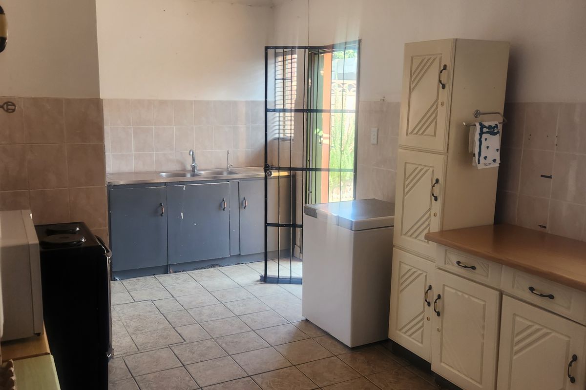 Functional kitchen featuring tiled flooring, built-in cabinetry, a double sink, and a security gate leading to the exterior.