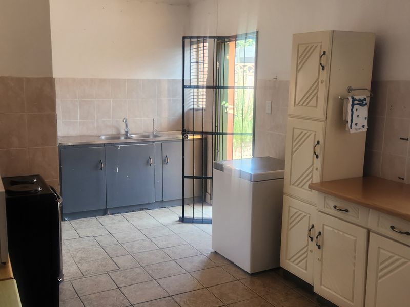 Functional kitchen featuring tiled flooring, built-in cabinetry, a double sink, and a security gate leading to the exterior.