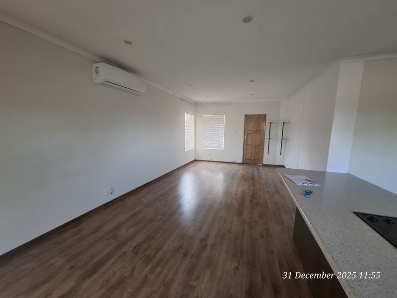 Spacious open-plan living area featuring laminate flooring, recessed lighting, and a wall-mounted air conditioning unit, offering a clean and versatile layout.