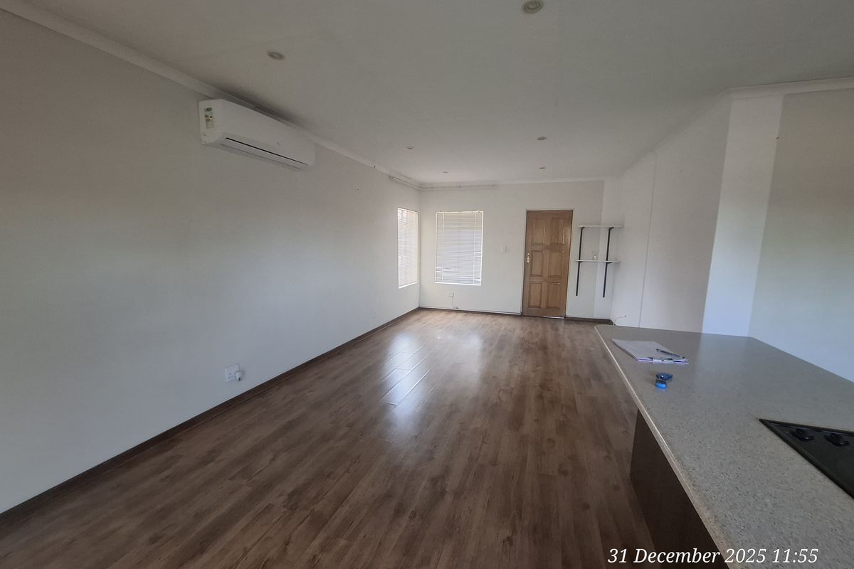 Spacious open-plan living area featuring laminate flooring, recessed lighting, and a wall-mounted air conditioning unit, offering a clean and versatile layout.