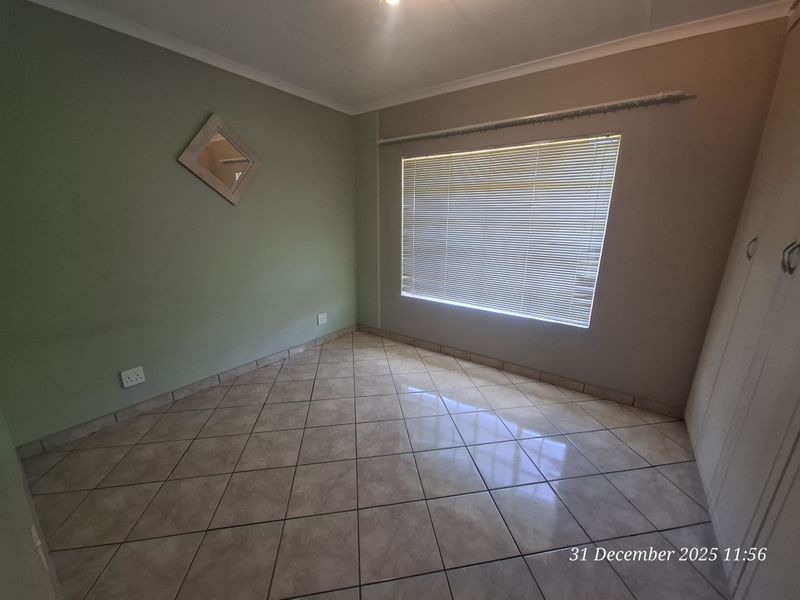 An empty bedroom featuring tiled flooring, built-in cupboards, and venetian blinds, providing a clean and neutral space ready for personalization.