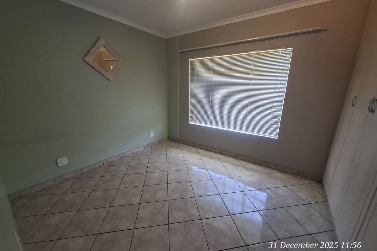 An empty bedroom featuring tiled flooring, built-in cupboards, and venetian blinds, providing a clean and neutral space ready for personalization.
