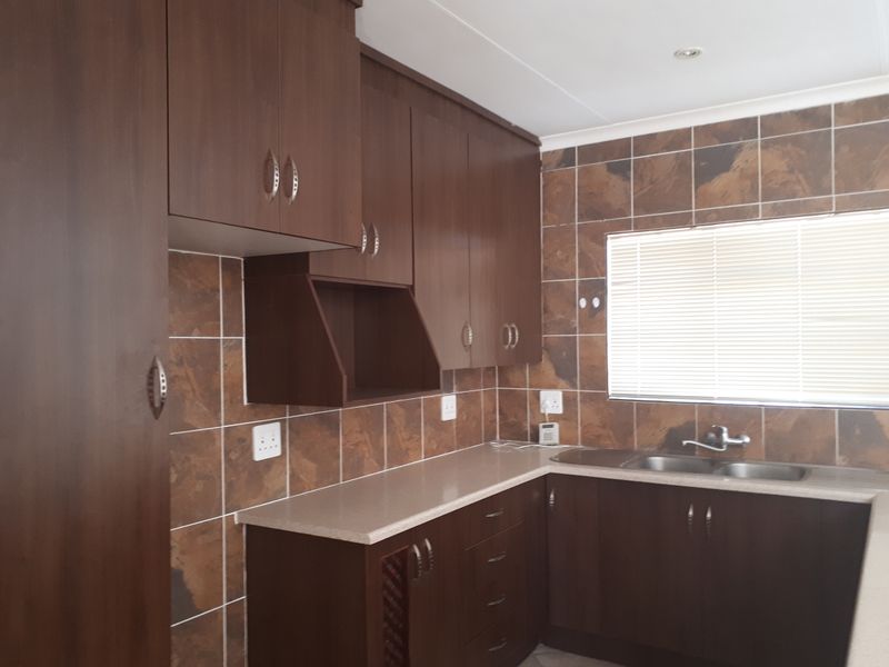 A functional kitchen featuring dark wood-look cabinetry, stone-tiled backsplash, and a double stainless steel sink with ample counter space.