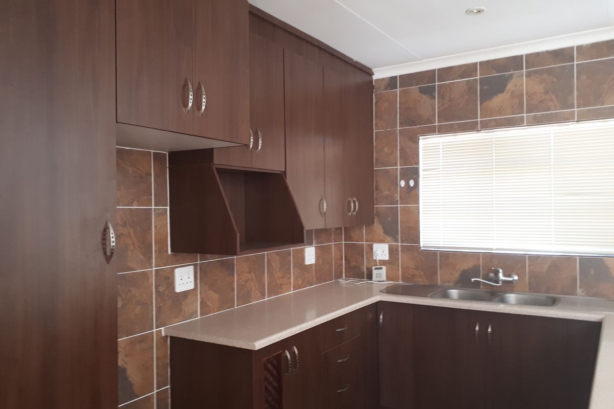 A functional kitchen featuring dark wood-look cabinetry, stone-tiled backsplash, and a double stainless steel sink with ample counter space.