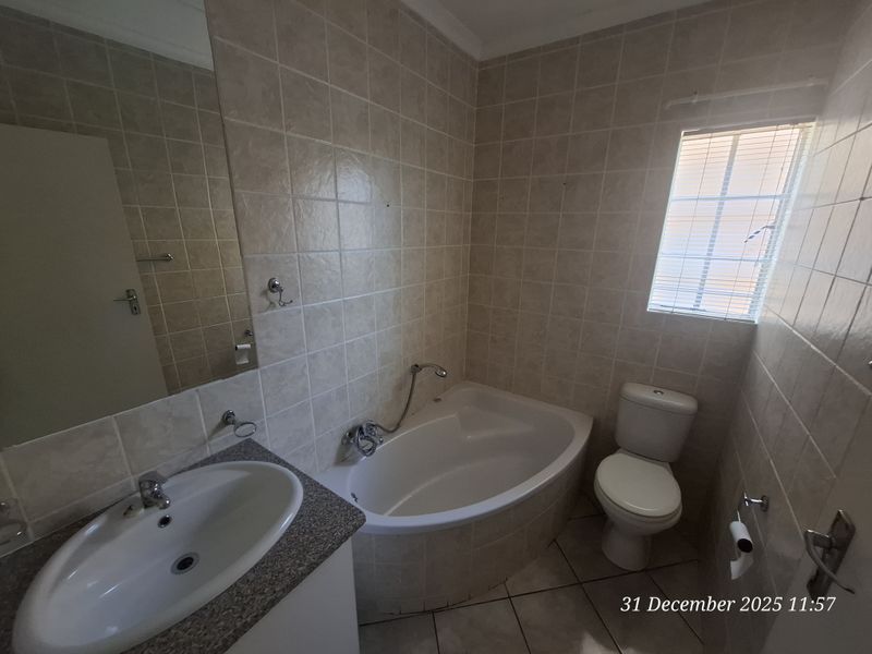 A functional bathroom featuring a corner bathtub, built-in vanity with basin, toilet, and neutral wall tiling.
