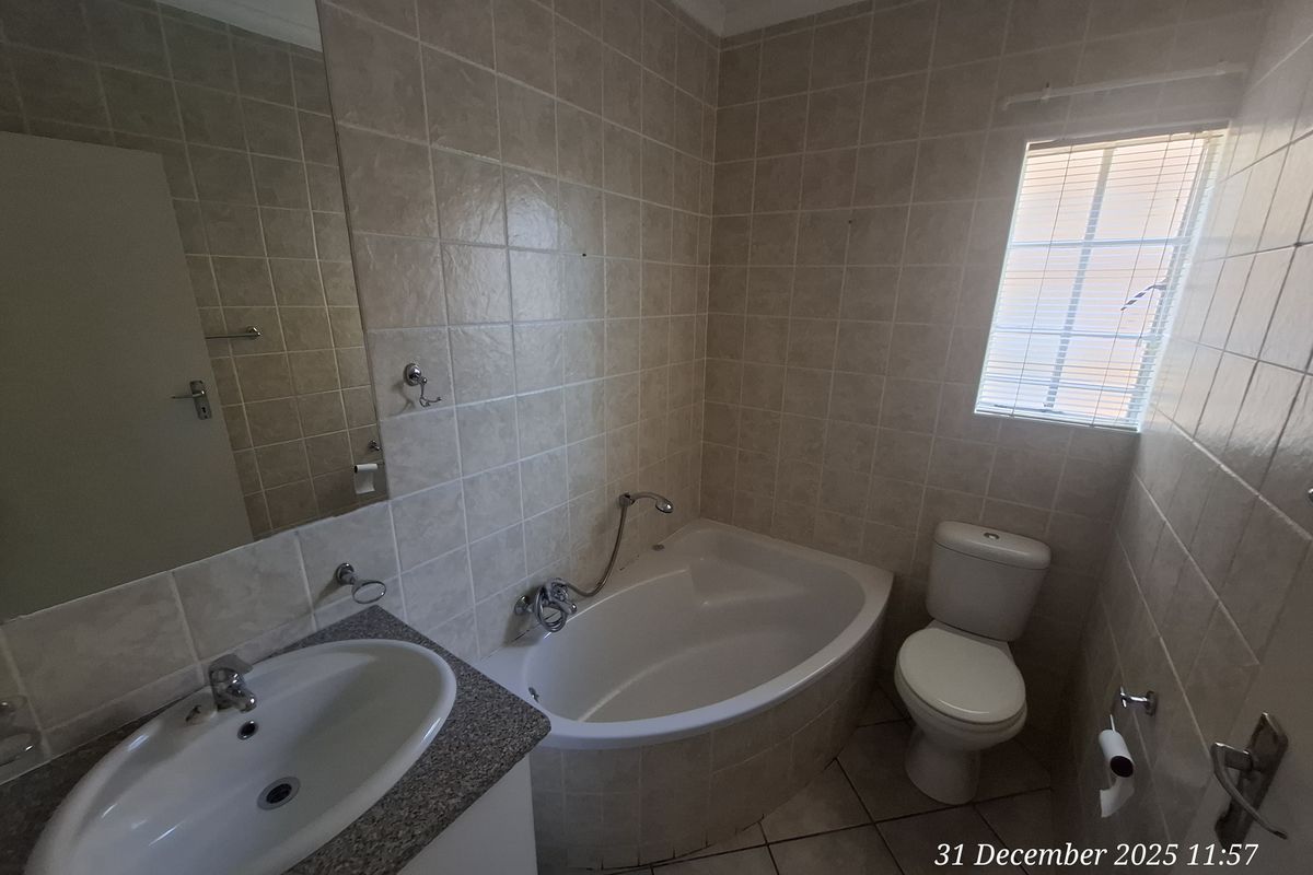 A functional bathroom featuring a corner bathtub, built-in vanity with basin, toilet, and neutral wall tiling.