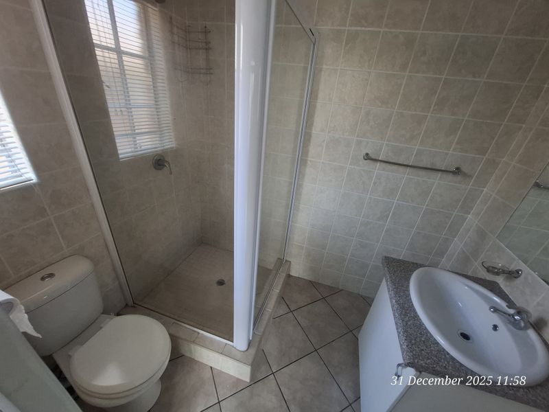 A functional bathroom featuring a shower enclosure, vanity with basin, and neutral wall and floor tiling.