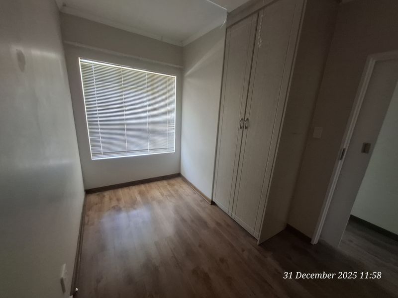 A clean, empty bedroom featuring laminate flooring, built-in cupboards, and venetian blinds, offering a neutral space ready for personalization.
