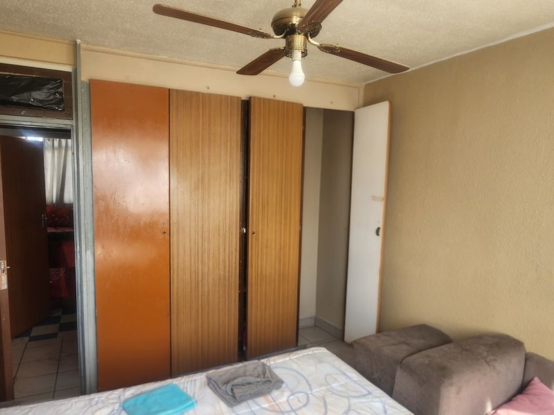 Bedroom featuring built-in wooden cupboards and a ceiling fan, requiring cosmetic updates to modernize the space.