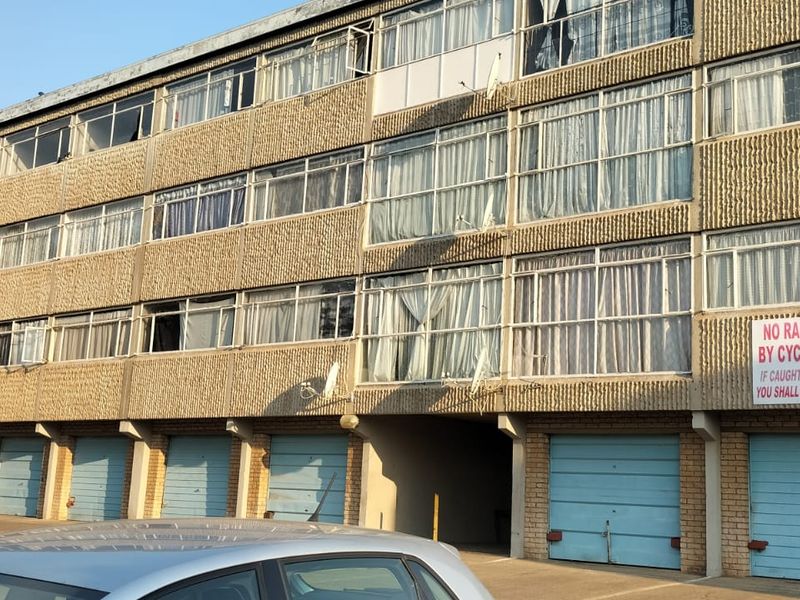 Exterior view of a multi-story apartment block featuring a concrete facade, multiple windows, and a row of ground-level garage doors.