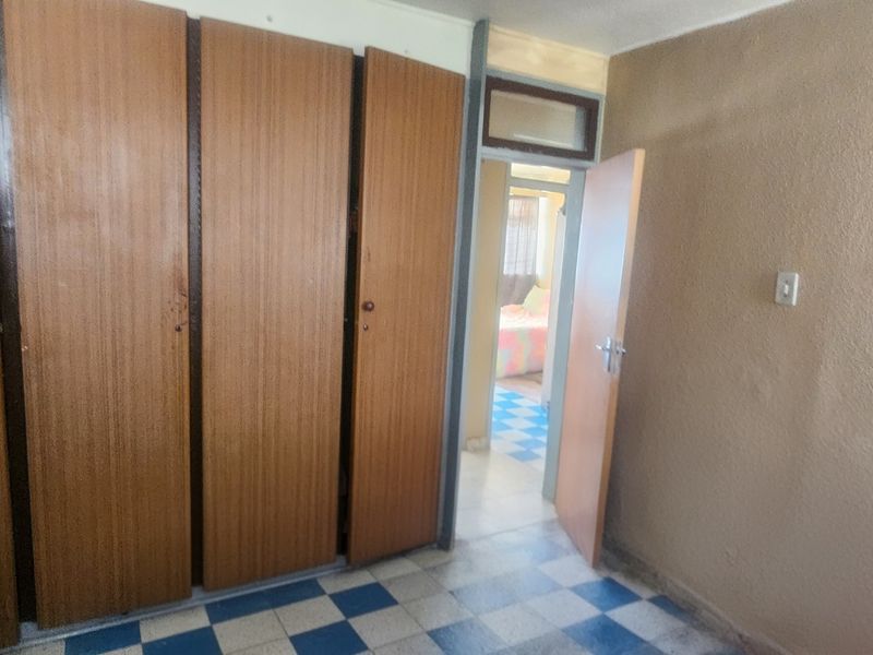 A bedroom featuring built-in wooden cupboards and tiled flooring, offering a functional space ready for modernization.