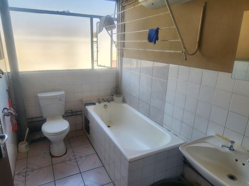 A dated bathroom featuring a standard bathtub, toilet, and washbasin with tiled finishes, requiring renovation to modernize the space.