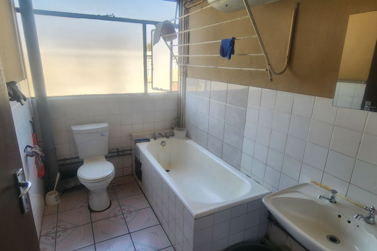 A dated bathroom featuring a standard bathtub, toilet, and washbasin with tiled finishes, requiring renovation to modernize the space.