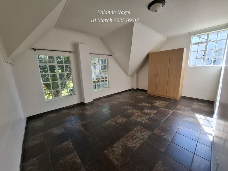 A spacious bedroom featuring vaulted ceilings, dark tiled flooring, and built-in wardrobe storage, offering a bright and versatile living space.