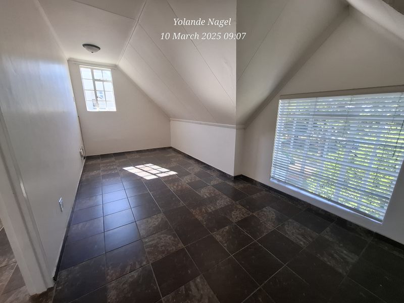 An empty bedroom featuring dark tiled flooring, sloped ceilings, and natural light from multiple windows with fitted blinds.