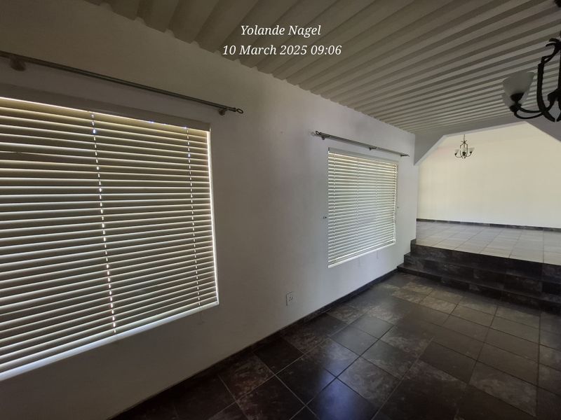 An empty living area featuring dark tiled flooring, stepped floor transition, and natural light provided by windows with fitted venetian blinds.