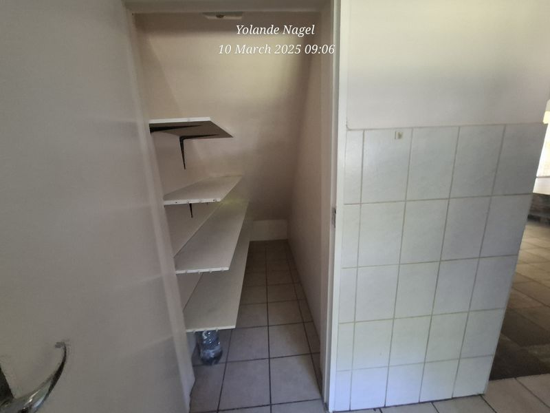 A small utility or pantry area featuring built-in shelving, tiled flooring, and a tiled wall section.