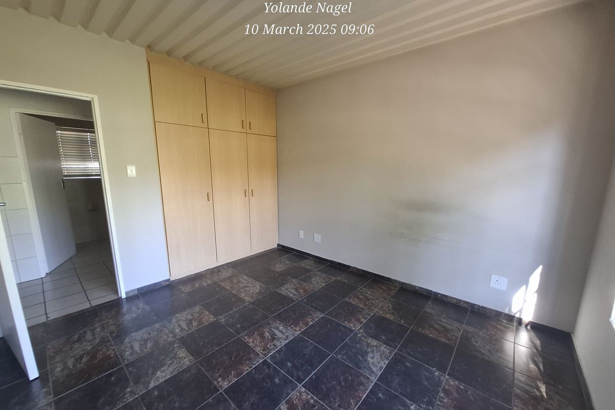 An empty bedroom featuring dark tiled flooring, built-in wooden cupboards, and a corrugated metal ceiling, with an adjacent doorway leading to another room.