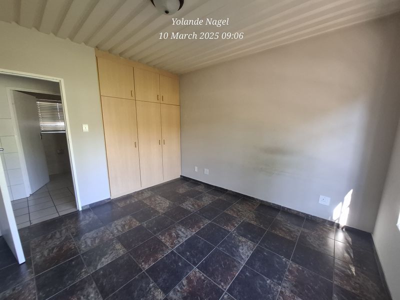 An empty bedroom featuring dark tiled flooring, built-in wooden cupboards, and a corrugated metal ceiling, with an adjacent doorway leading to another room.
