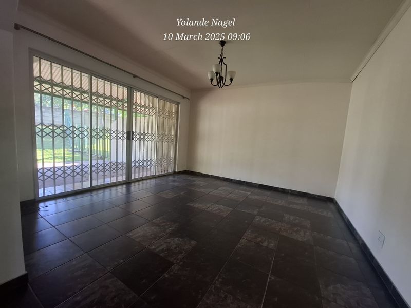 Spacious, empty living room featuring dark tiled flooring, a central light fixture, and large sliding glass doors with security gates leading to the garden.