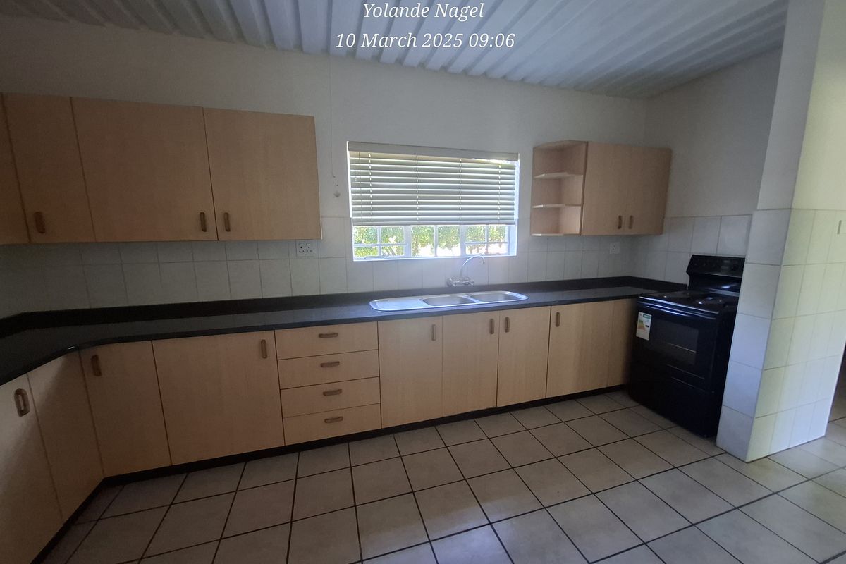 A functional kitchen featuring light wood-tone cabinetry, dark countertops, tiled flooring, and a built-in sink area with a window view.