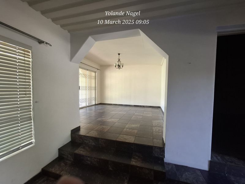 An empty, split-level living area featuring dark tiled flooring, a sliding glass door with security gate, and neutral wall finishes.