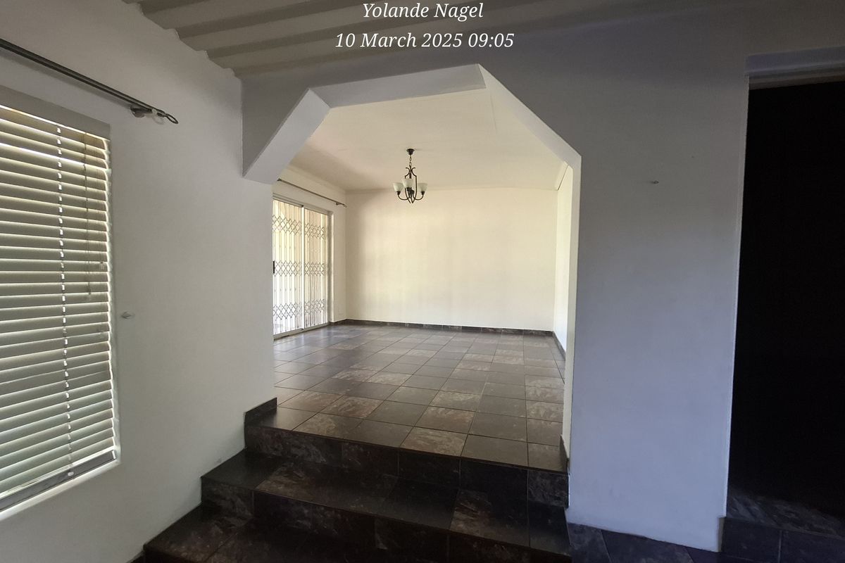 An empty, split-level living area featuring dark tiled flooring, a sliding glass door with security gate, and neutral wall finishes.