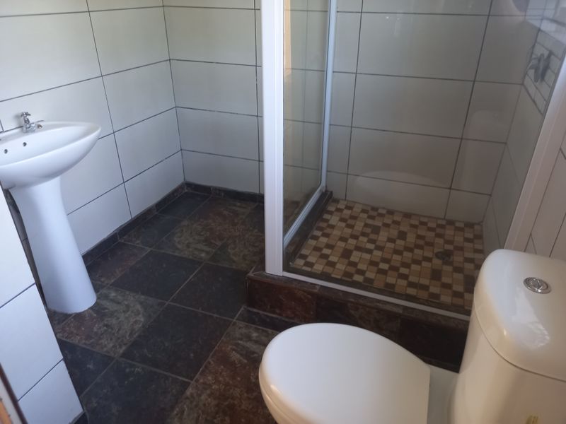 A functional bathroom featuring a pedestal basin, a separate shower enclosure with tiled flooring, and a standard toilet with white wall tiling.