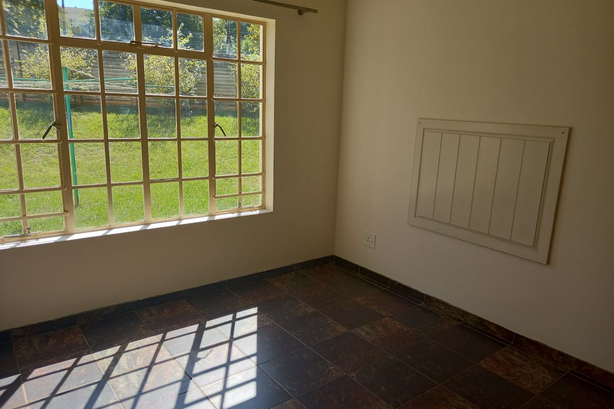 A bright, empty bedroom featuring tiled flooring and a large multi-pane window overlooking the garden.