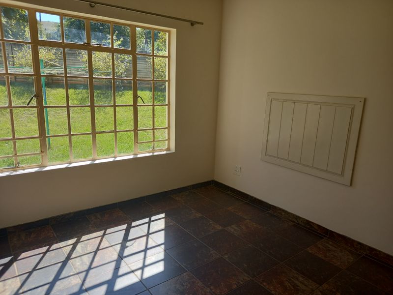 A bright, empty bedroom featuring tiled flooring and a large multi-pane window overlooking the garden.