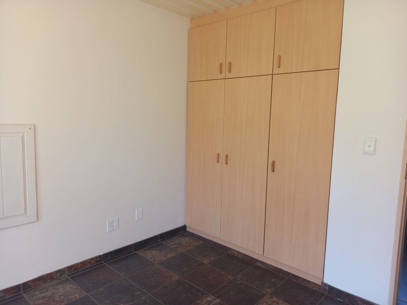 A clean, empty bedroom featuring light wood-finish built-in cupboards and dark tiled flooring, providing a neutral space ready for personalization.
