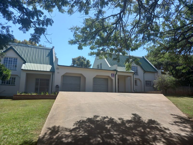 Front elevation of a double-story house featuring a double garage, concrete driveway, and green metal roofing set within a landscaped garden.