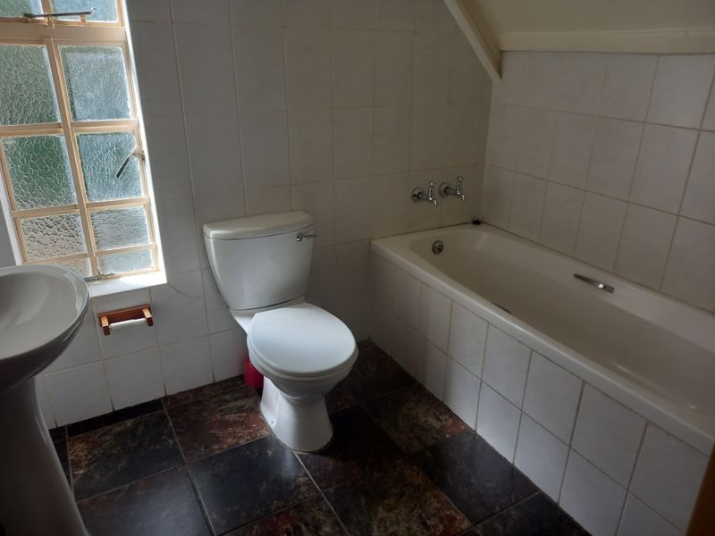 A functional bathroom featuring a pedestal basin, toilet, and built-in bathtub with tiled finishes throughout.