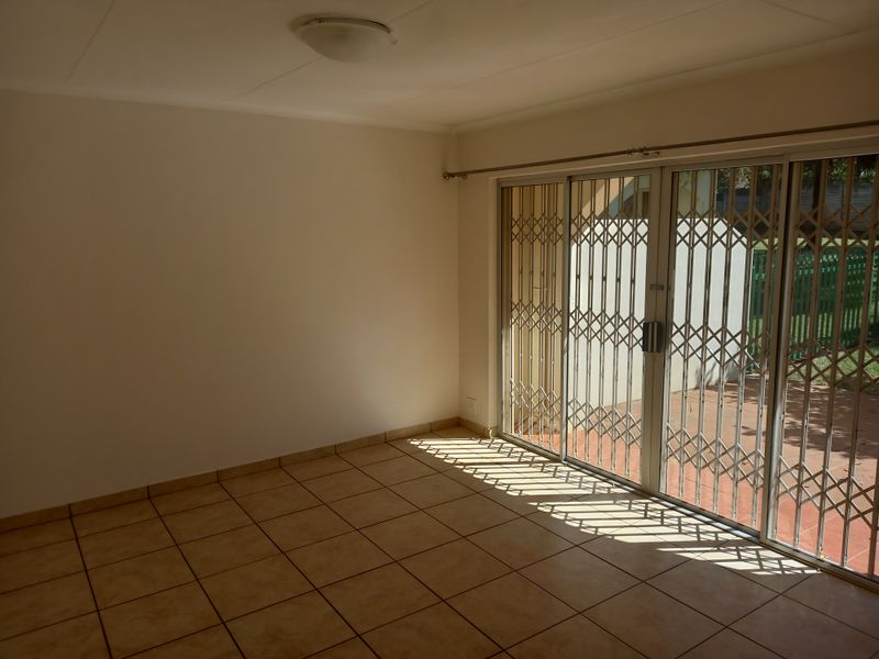 An empty living room featuring tiled flooring and large sliding glass doors with a security gate, providing direct access to the outdoor area.