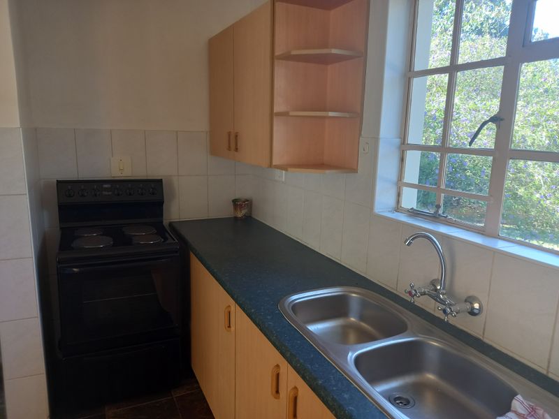 A functional kitchen featuring built-in cabinetry, laminate countertops, a double bowl sink, and a freestanding electric stove with tiled splashbacks.