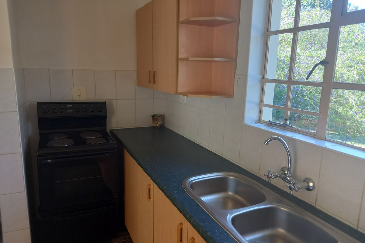 A functional kitchen featuring built-in cabinetry, laminate countertops, a double bowl sink, and a freestanding electric stove with tiled splashbacks.