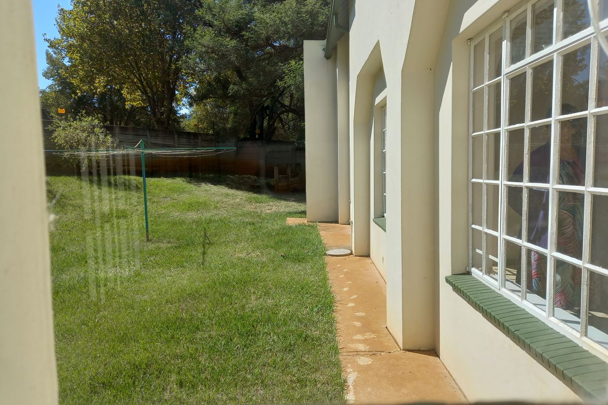 A view of the rear garden and lawn area, featuring a concrete pathway along the side of the house with lattice windows.