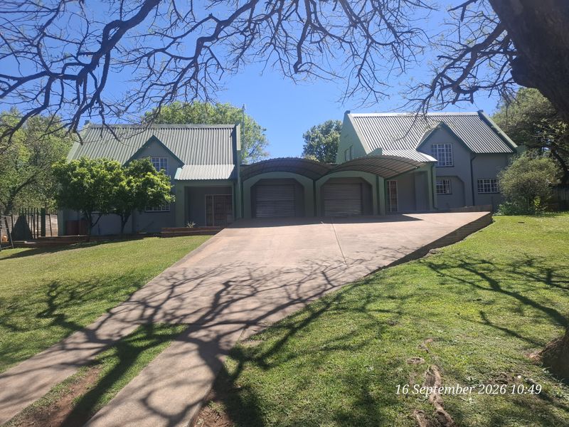 Front view of a residential property featuring a double garage, concrete driveway, and a large landscaped garden area.