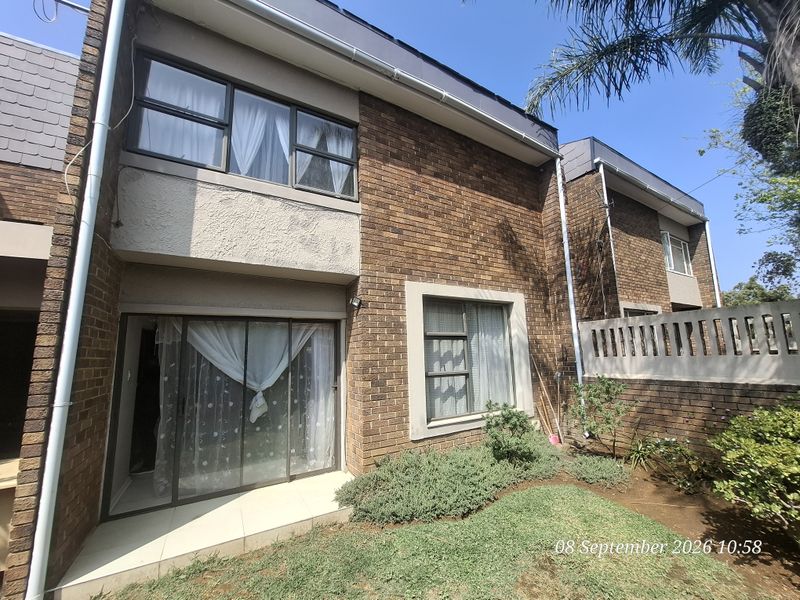 Rear view of a double-storey townhouse featuring face brick construction, a small patio area, and a private garden space.