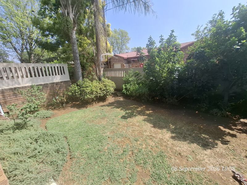 A private rear garden area featuring a lawn, established trees, and a brick boundary wall with a concrete balustrade.
