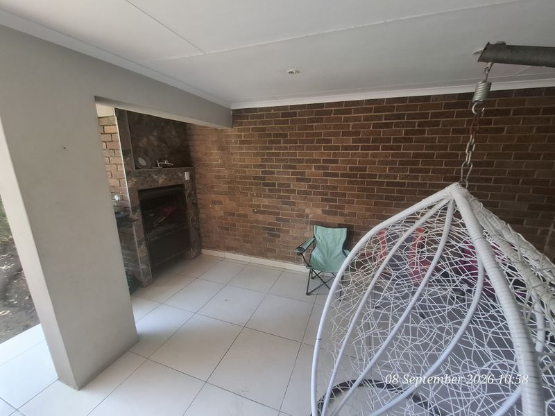 Covered patio area featuring a built-in braai, tiled flooring, and an exposed brick feature wall, ideal for outdoor entertaining.