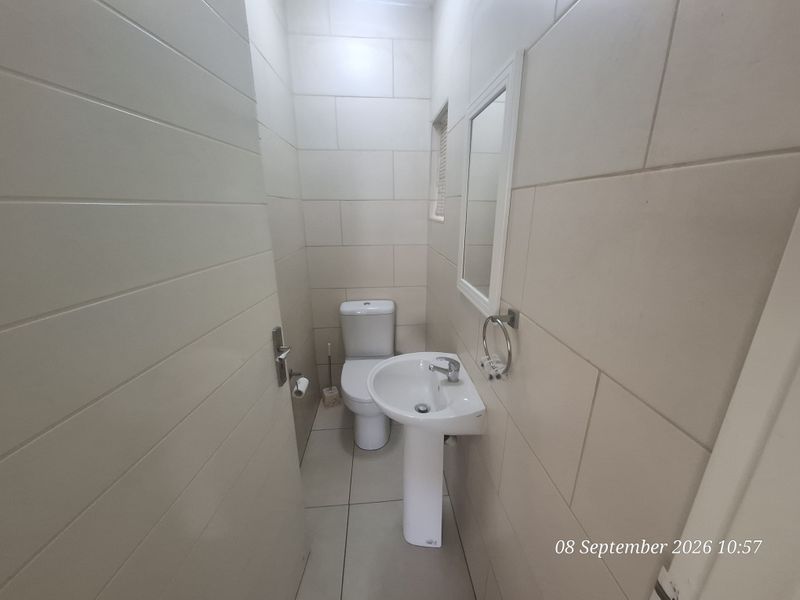 A clean and functional guest bathroom featuring a pedestal basin, toilet, and neutral wall and floor tiling.