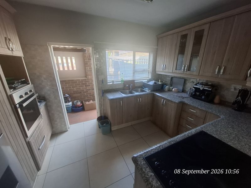 Functional kitchen featuring laminate cabinetry, granite countertops, built-in oven, and electric hob, with direct access to an outdoor area.