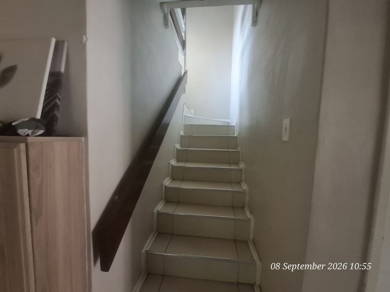A functional tiled staircase featuring a wooden handrail, providing access between levels within the townhouse.
