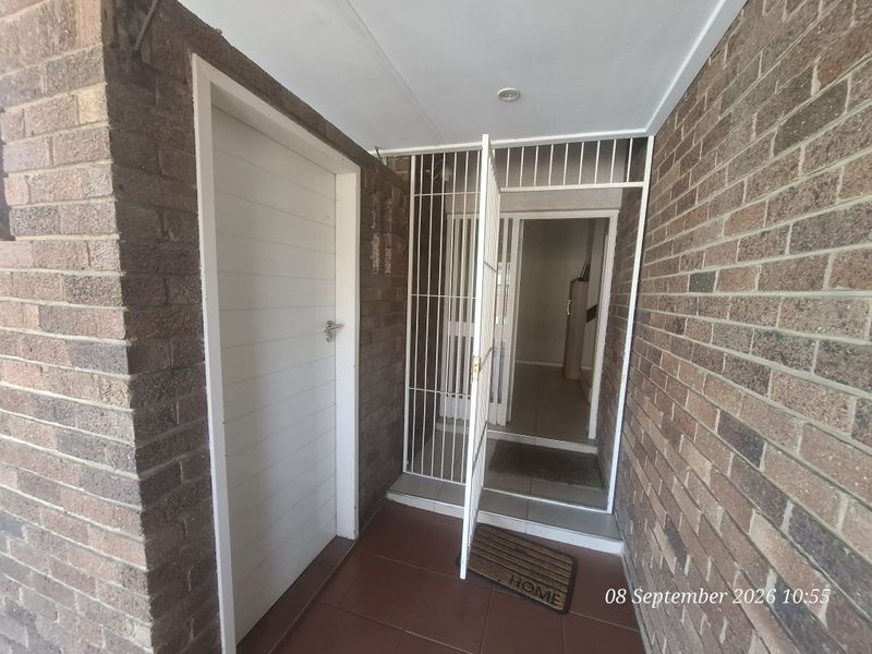 A secure townhouse entrance featuring a brick facade, tiled flooring, and a white security gate leading into the home.