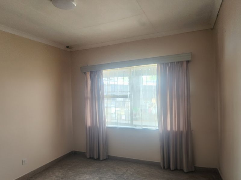 An empty bedroom featuring a window with security bars, neutral walls, and a ceiling light fixture.
