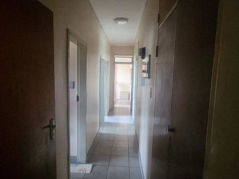 A functional residential hallway featuring tiled flooring, built-in storage cupboards, and access to multiple rooms.