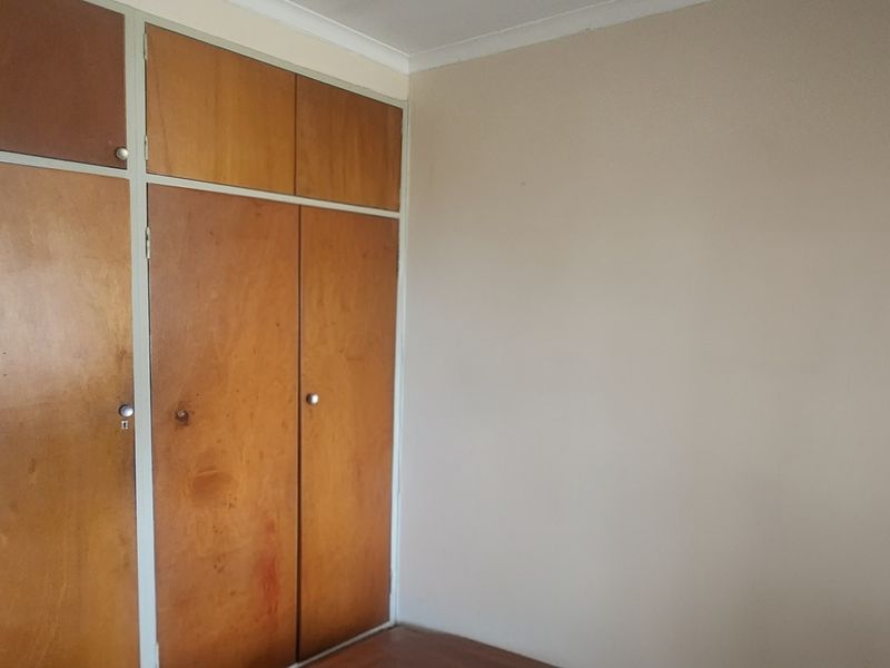 A vacant bedroom featuring built-in wooden cupboards and neutral wall finishes, offering a blank canvas for potential interior updates.